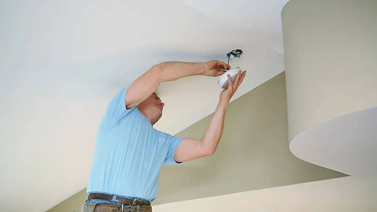 Electrician fitting a ceiling smoke alarm in a Sydney home
